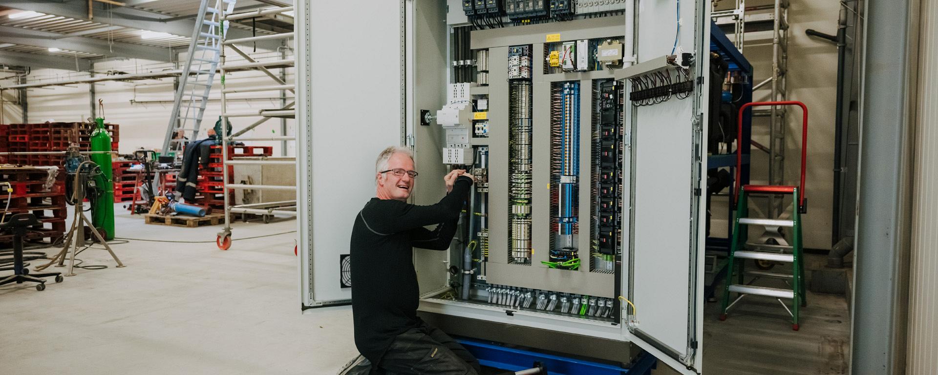 Een monteur werkt aan een open schakelkast in een werkplaats.