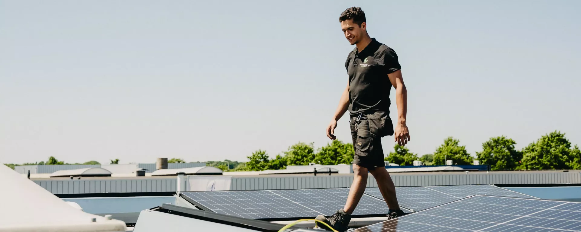 Monteur van Waasdorp E-Techniek loopt over zonnepanelen op een plat dak tijdens installatie op een zonnige dag.
