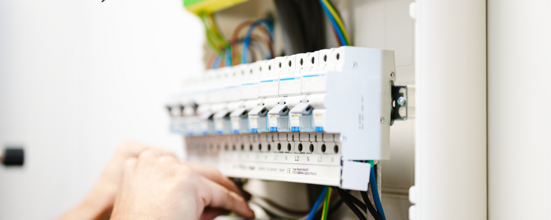 Close-up van handen die werken aan een elektrische verdeelkast, met zicht op bedrading, schakelaars en componenten in een nette installatie.