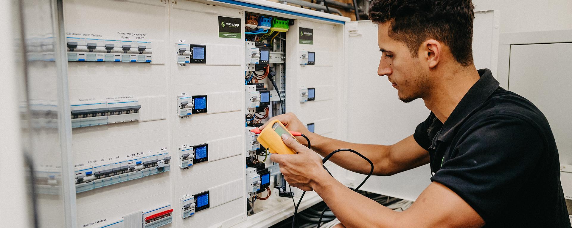 Monteur van Waasdorp test bedrading in groepenkast met meetapparaat tijdens elektrotechnisch onderhoud.