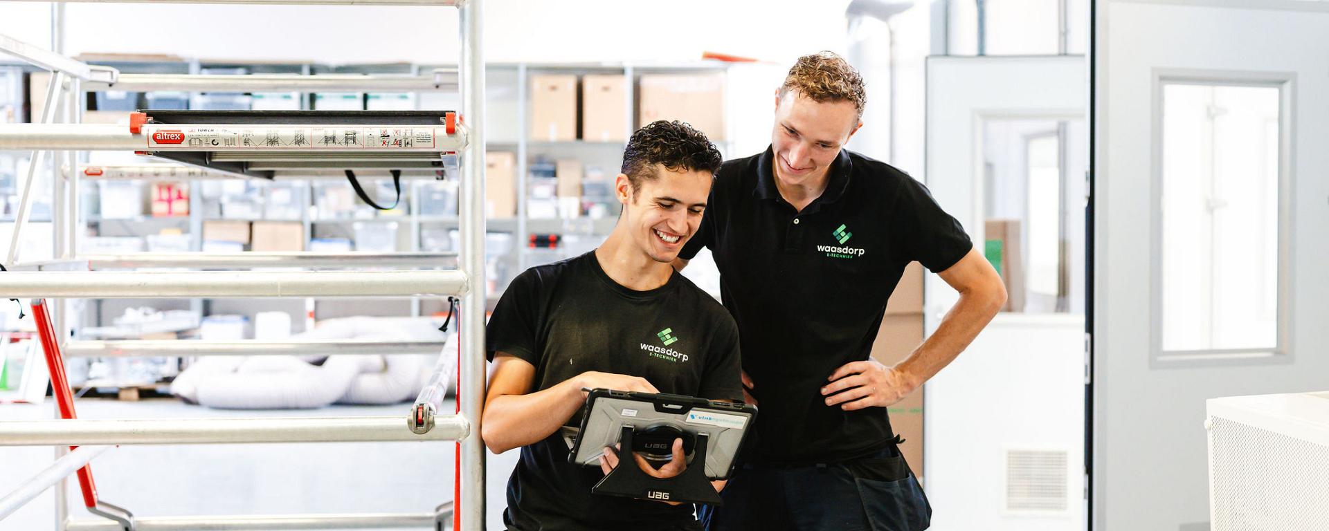 Monteur van Waasdorp met meetapparatuur en tablet in werkruimte, klaar voor elektrotechnische controle.