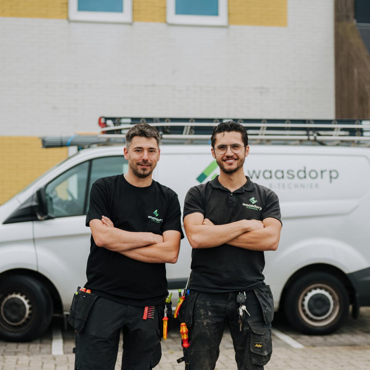 Twee medewerkers van bedrijf Waasdorp staan met gekruiste armen voor een bedrijfsbus.