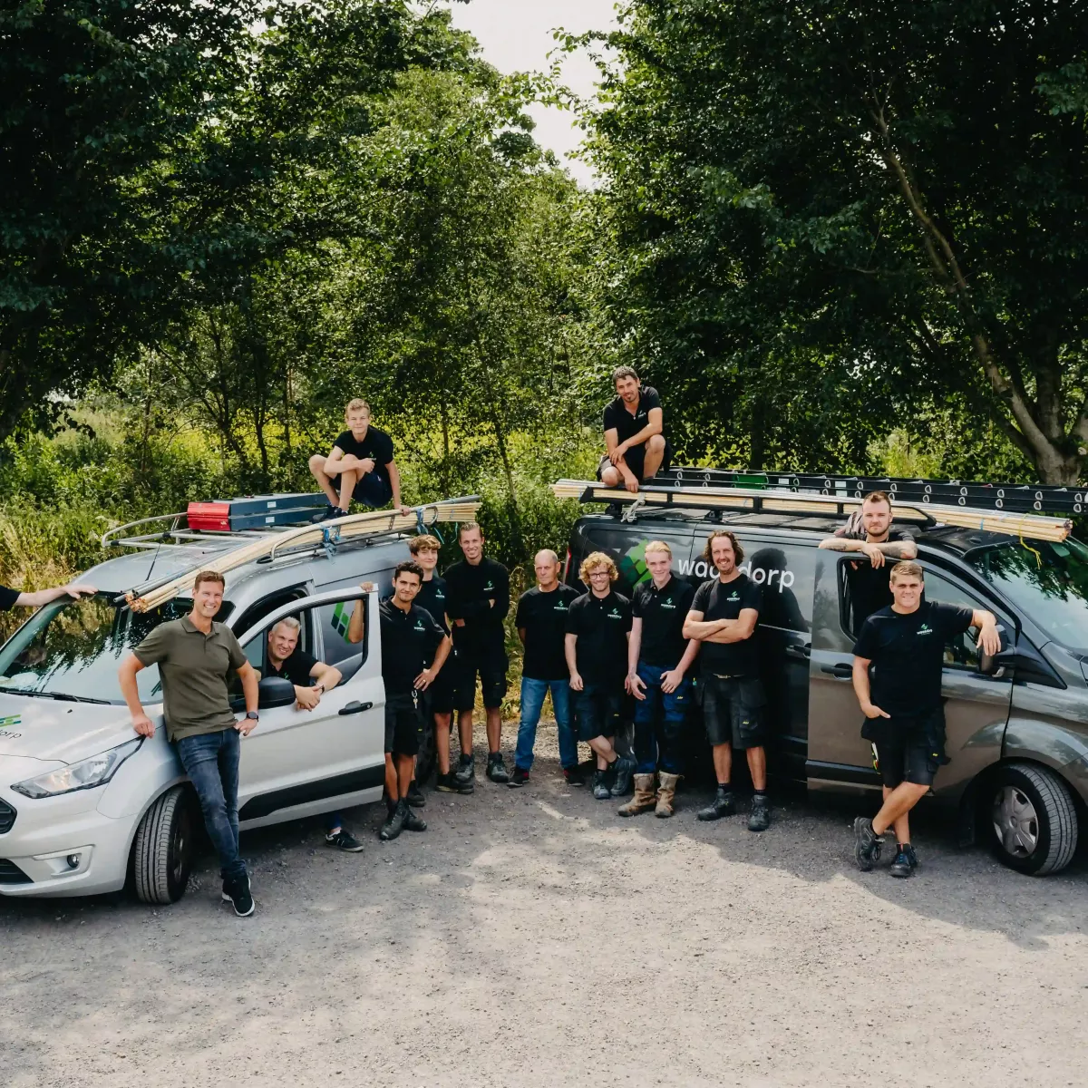 Teamfoto van Waasdorp E-Techniek met medewerkers rondom twee bedrijfsbussen in een groene buitenomgeving.