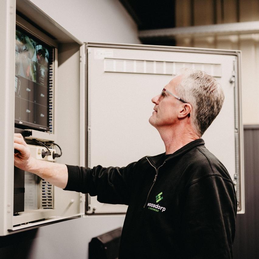 ChatGPT zei:  Monteur van Waasdorp controleert beeldscherm en schakelkast in industriƫle installatie.