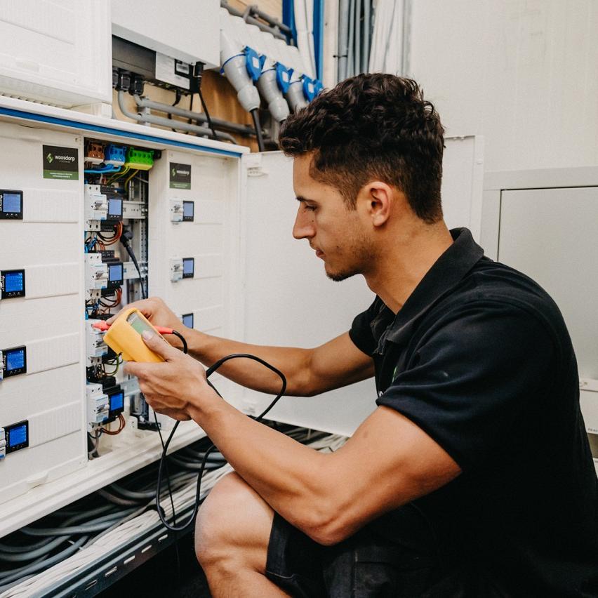 Monteur van Waasdorp test bedrading in groepenkast met meetapparaat tijdens elektrotechnisch onderhoud.