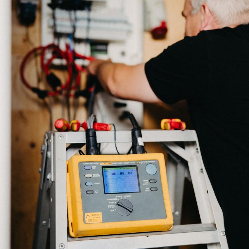 Monteur van Waasdorp voert metingen uit in groepenkast, meetapparaat staat op ladder.