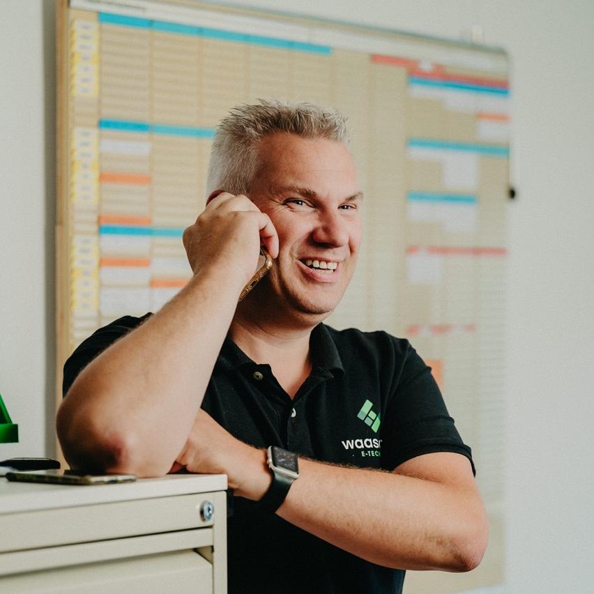 Monteur van Waasdorp voert telefonisch overleg op kantoor met planbord op de achtergrond.