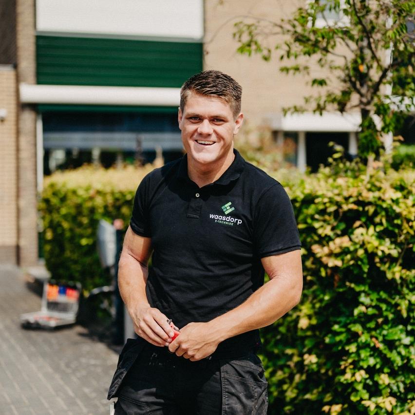 Monteur van Waasdorp buiten aan het werk bij een woning, lachend in werkkleding.