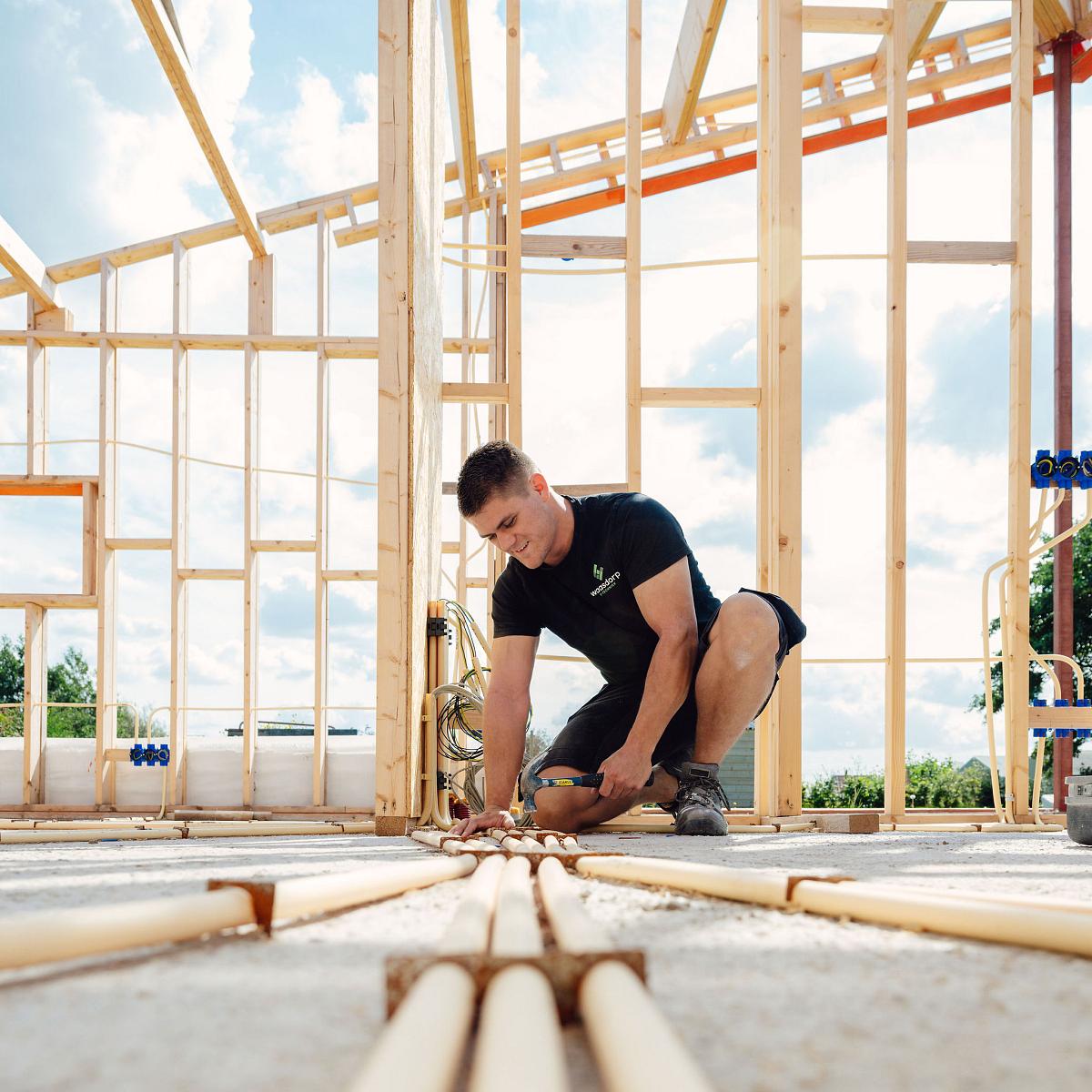 Monteur legt leidingen aan op de vloer van een woning in aanbouw.