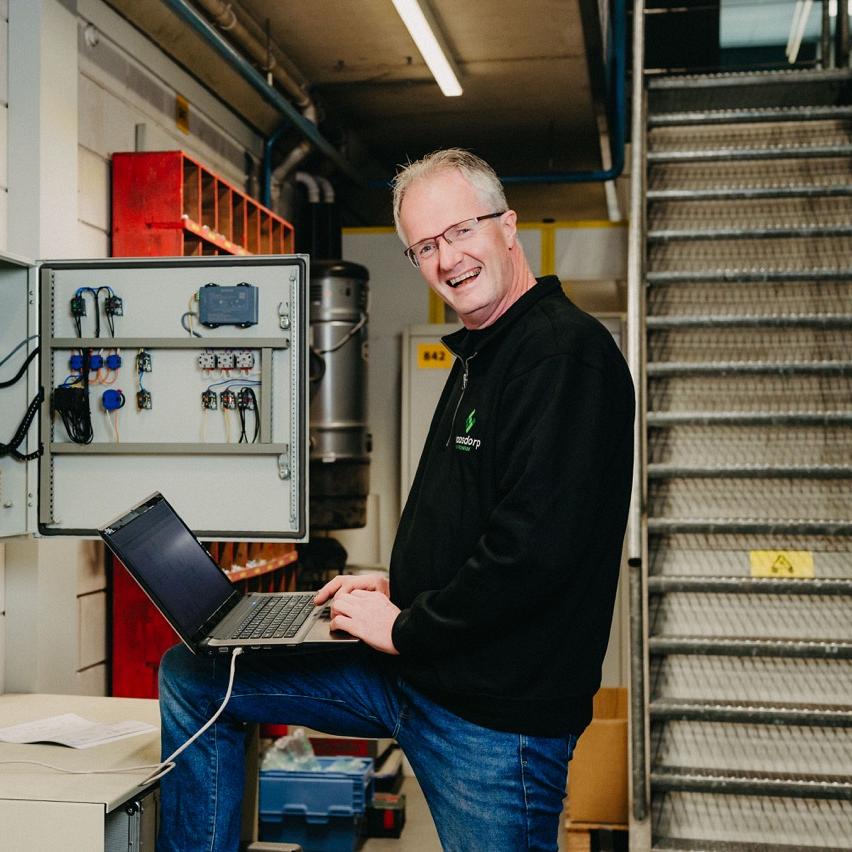 Monteur van Waasdorp voert controle uit op schakelkast met laptop in industriële omgeving.