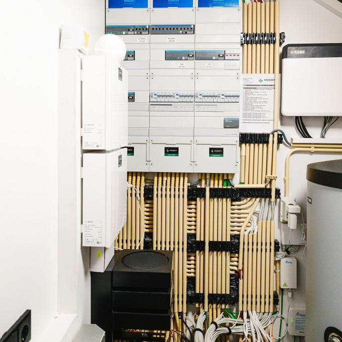 Overzicht van een technische ruimte met elektrische verdeelkasten, netjes georganiseerde kabels en aangesloten apparatuur voor energie- en klimaatbeheersing.