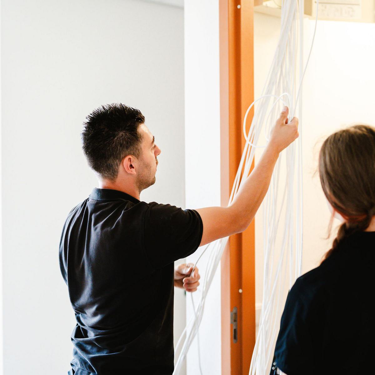 Monteur werkt aan bekabeling in technische ruimte terwijl collega meekijkt