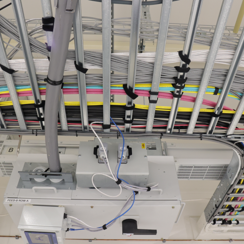 Overzicht van een technische installatie met kleurrijke kabelbundels georganiseerd in metalen goten, elektrische aansluitingen en apparatuur voor stroomverdeling.