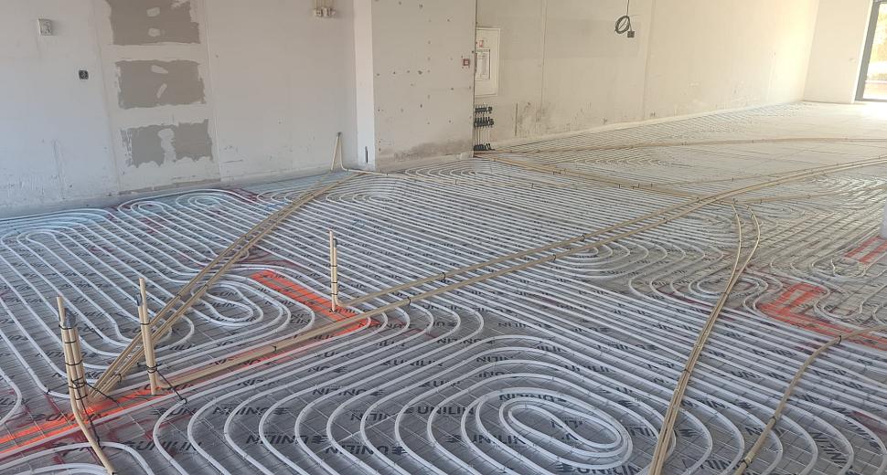 Vloerverwarmingssysteem in een nieuwbouwruimte, met duidelijk zichtbare buizen in cirkelvormig patroon over een isolatielaag, klaar voor afwerking.