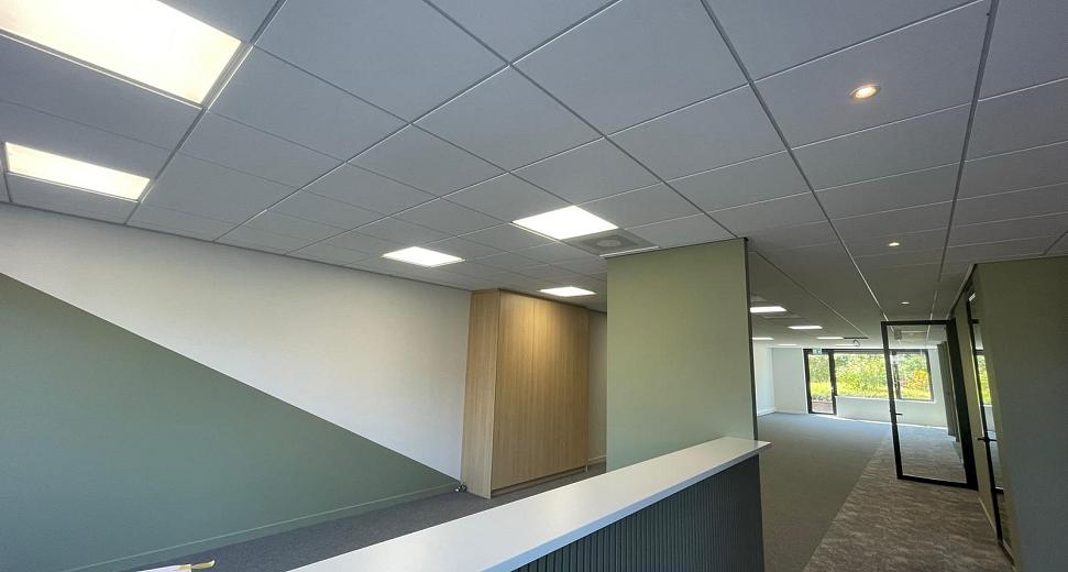 Modern kantoorinterieur met een strakke balie, verlaagd systeemplafond met inbouwverlichting, groene wanden en een glazen deur naar een lichte vergaderruimte.