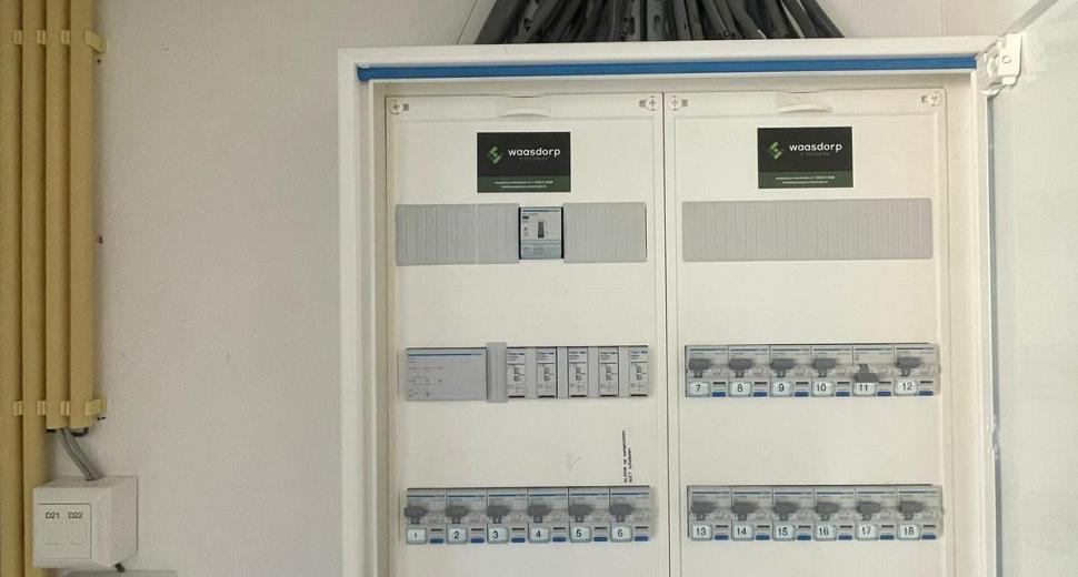 Elektriciteitskast met gestructureerde bedrading en schakelaars, voorzien van Waasdorp-logo’s, en diverse stroomgroepen voor gebouwbeheer en installatie.