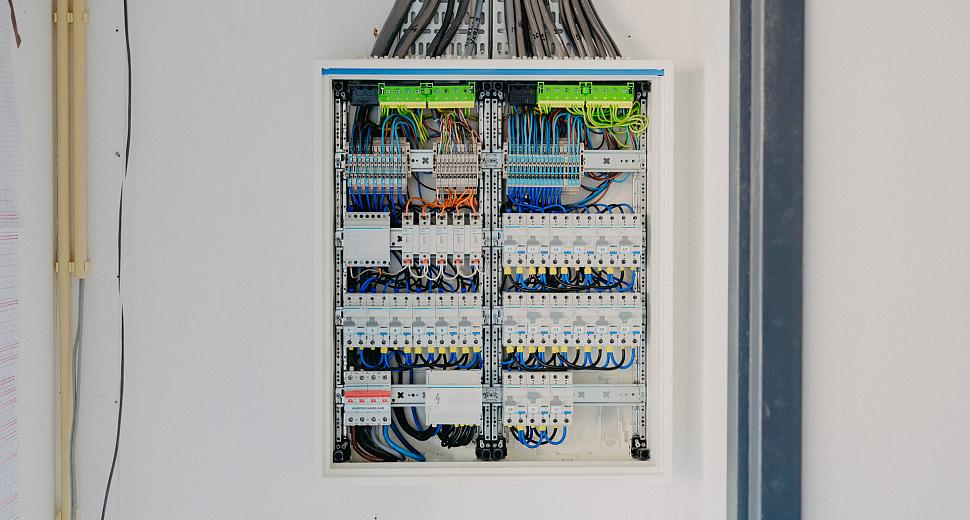 Open elektriciteitskast met geordende bedrading, schakelaars en verdeelmodules, geïnstalleerd tegen een witte muur in een technische ruimte.