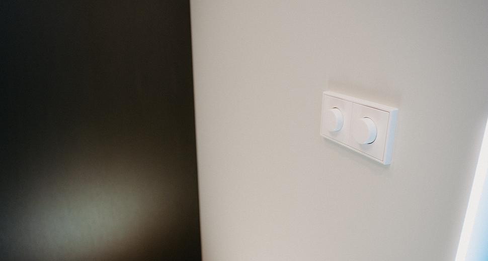 Witte wand met een dubbele lichtdimmer gemonteerd, naast een zwart paneel, in een modern interieur met strakke afwerking.