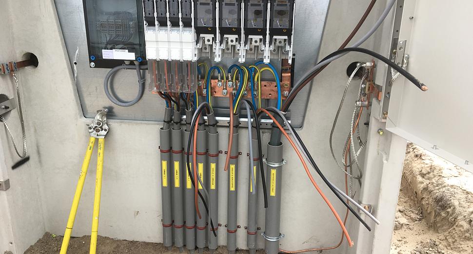 Open elektrisch verdeelstation met zichtbare bekabeling en zekeringen, waarbij diverse stroomkabels netjes zijn aangesloten op de verbindingspunten.