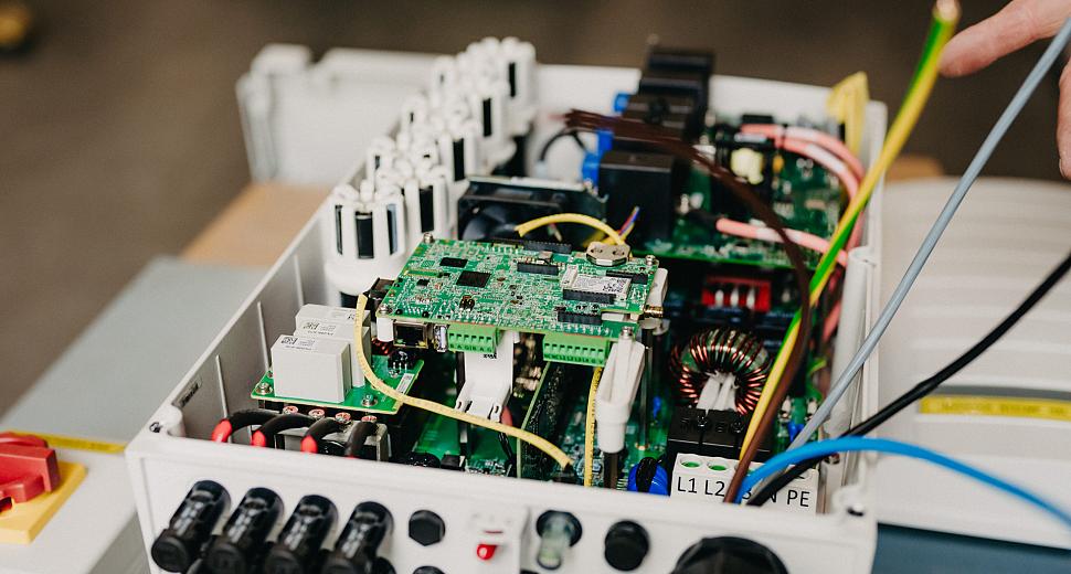  Interne componenten van een geopende SolarEdge omvormer, met zicht op de printplaat, bedrading en elektrische aansluitingen, op een werkblad in een magazijn.