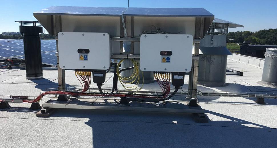 Twee omvormers gemonteerd op een plat dak, aangesloten op zonnepanelen, met kabels netjes gebundeld en ventilatiesystemen op de achtergrond.