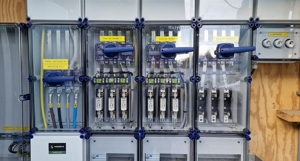 Elektriciteitskast met meerdere doorzichtige panelen, bedrading en schakelaars, gemonteerd tegen een houten achtergrond voor energiebeheer en distributie.