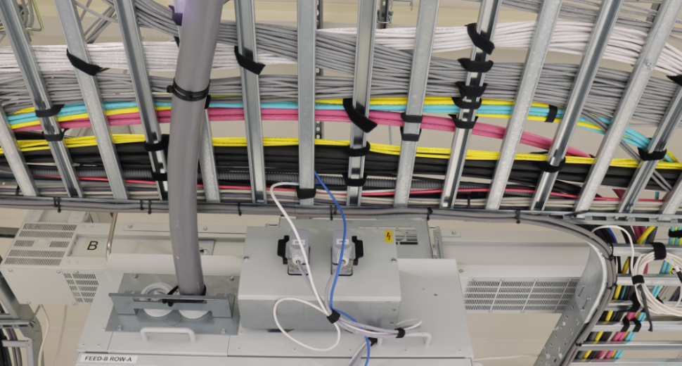 Overzicht van een technische installatie met kleurrijke kabelbundels georganiseerd in metalen goten, elektrische aansluitingen en apparatuur voor stroomverdeling.