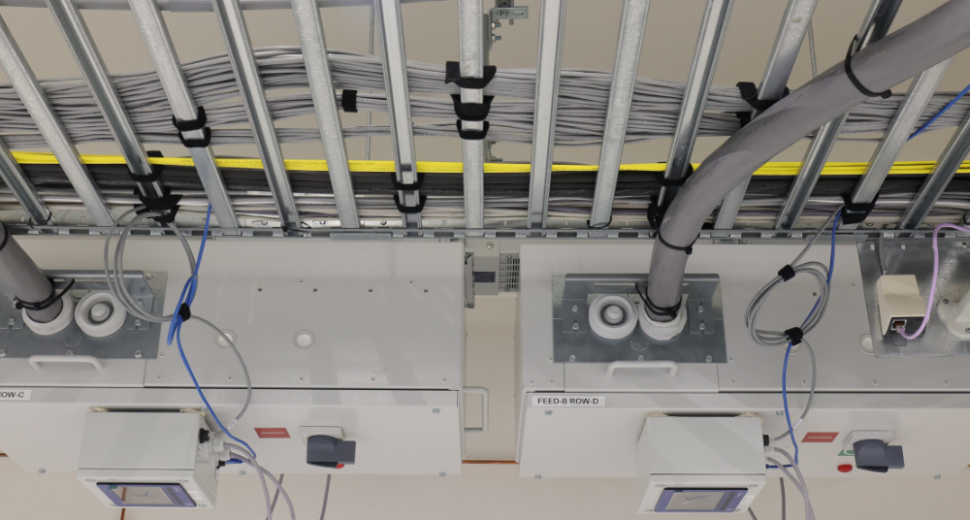 Technische installatie met metalen kabelgoten, geordende grijze kabels en aangesloten stroomverdeelkasten met aansluitpunten en apparatuur.
