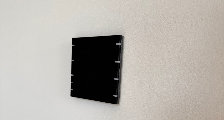 Zwart bedieningspaneel met vijf verticale touchzones, strak gemonteerd op een lichtgrijze muur, voor bediening van slimme functies in huis.