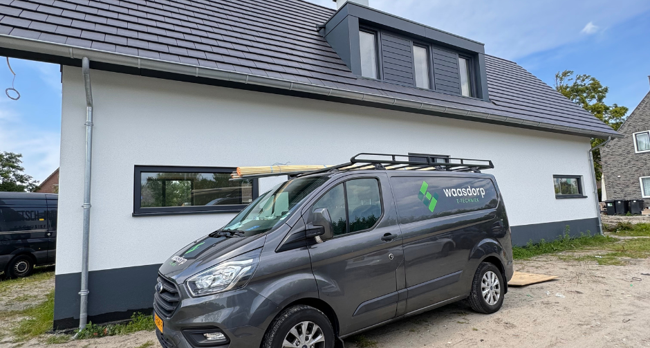 Grijze bedrijfswagen van Waasdorp E-Techniek geparkeerd voor een modern wit huis met donkere kozijnen en een schuin dak.