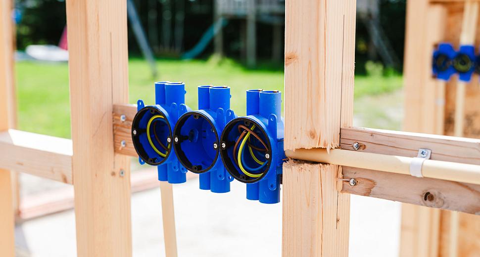 Close-up van blauwe inbouwdozen met aangesloten bedrading, bevestigd in een houten frame van een nieuwbouwproject.