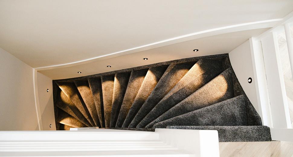 Wenteltrap met grijze bekleding, sfeervol verlicht door ingebouwde wandlampjes in een moderne, witte omgeving.