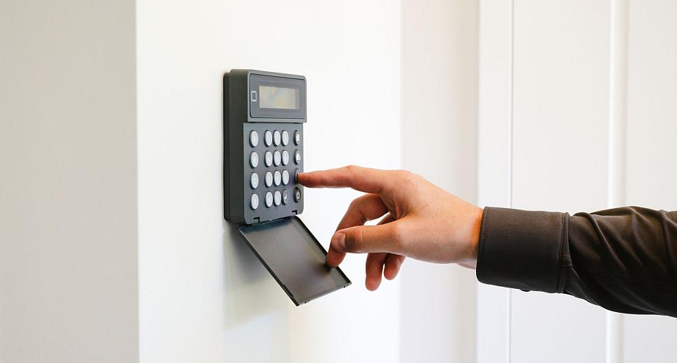  Hand bedient een zwart alarmsysteem met een numeriek toetsenbord en een klein scherm, gemonteerd op een witte muur.