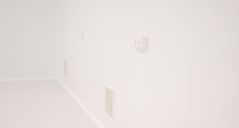 Witte muur in een minimalistische ruimte met een stopcontact en een ventilatierooster.