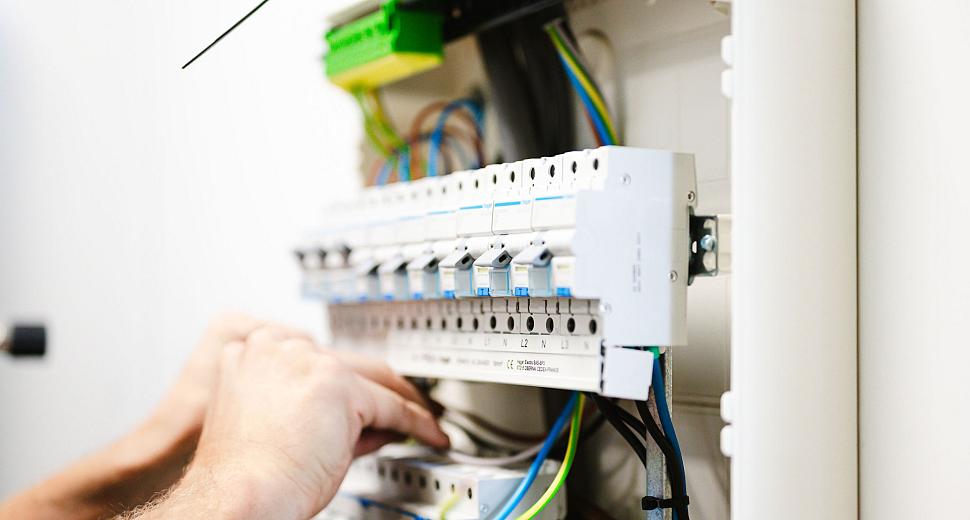 Close-up van handen die werken aan een elektrische verdeelkast, met zicht op bedrading, schakelaars en componenten in een nette installatie.