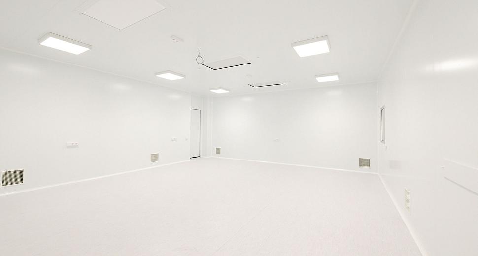 Lichte, volledig witte ruimte met ingebouwde verlichting in het plafond, ventilatieroosters in de muren en een gladde vloer, geschikt voor technische of steriele toepassingen.