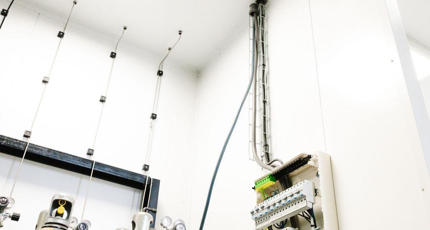 Elektrische installatie met een schakelkast en aangesloten bedrading aan een muur, naast gasflessen met regelapparatuur in een goed verlichte technische ruimte.
