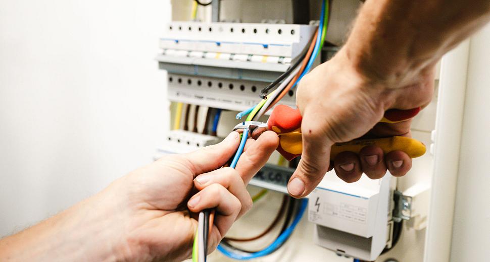 Close-up van twee handen die met gereedschap elektriciteitskabels knippen in een elektrische schakelkast. De bedrading wordt zorgvuldig bewerkt.