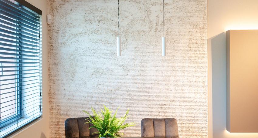 Ronde eettafel met een zwart tafelblad, omringd door bruine en grijze stoelen, een groene plant in het midden en een stijlvolle wand met lichte textuur.